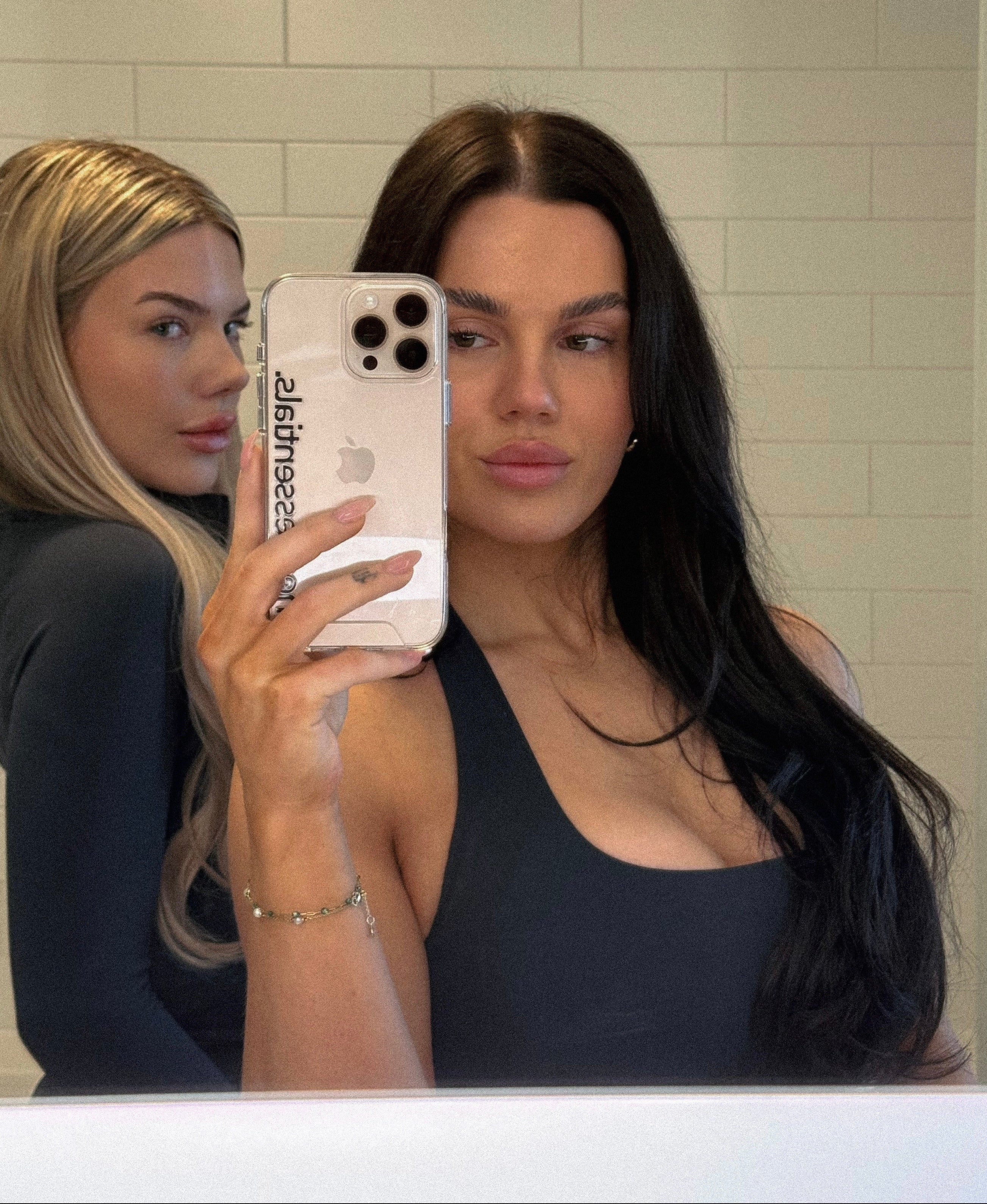 Two women taking a mirror selfie with a phone, one holding the phone.